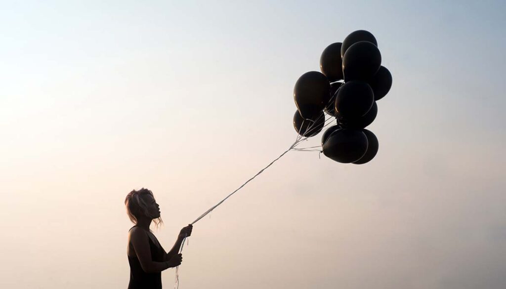 silhouette of woman at twilight letting go of black balloons 