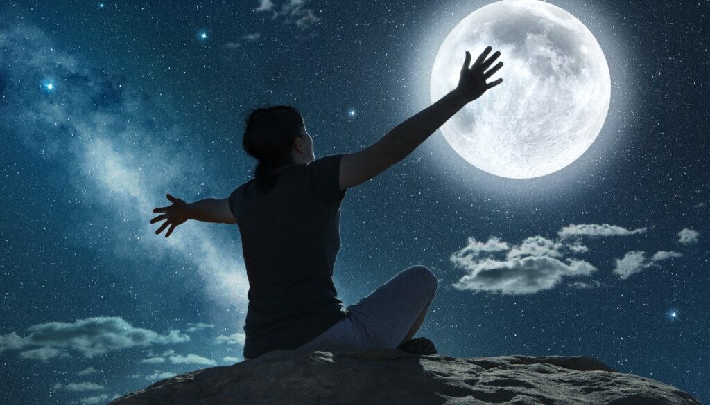 a person stretches out their arms while gazing at the moon