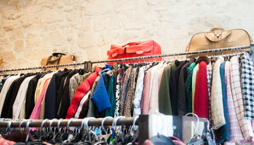 Racks of a thrift store with jackets, long sleeves, and purses