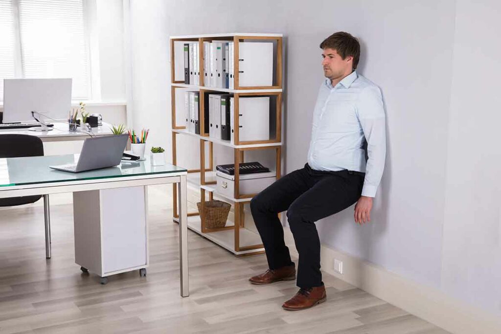 man doing wall sits in his office