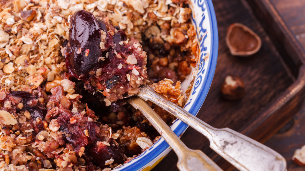 A bowl of plum crumble with two spoons 