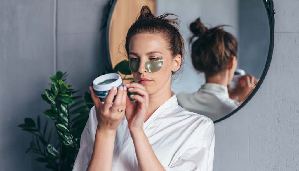woman reading label on skincare product while wearing under eye gel patches