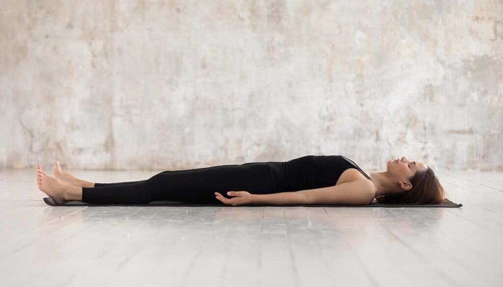 woman in relaxation yoga pose laying on floor with eyes closed