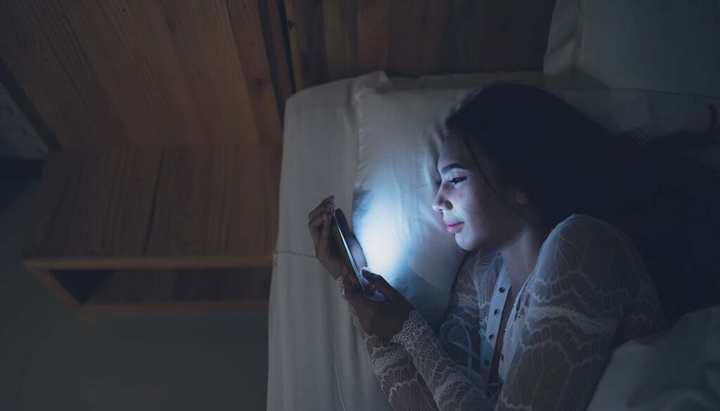 woman playing on her smartphone in bed at night
