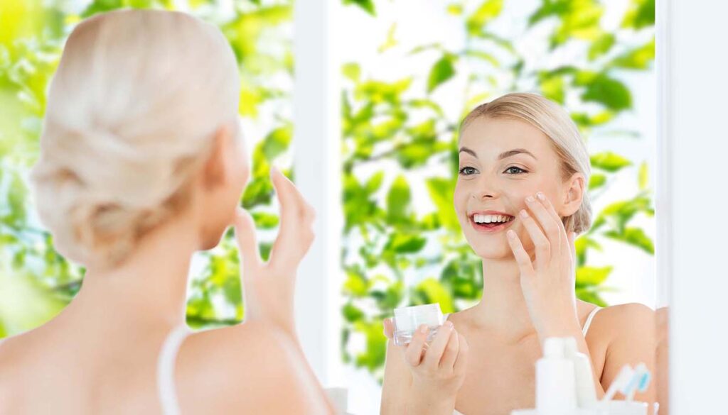 smiling woman doing skincare routine in bright and sunny room with lush greenery out the window