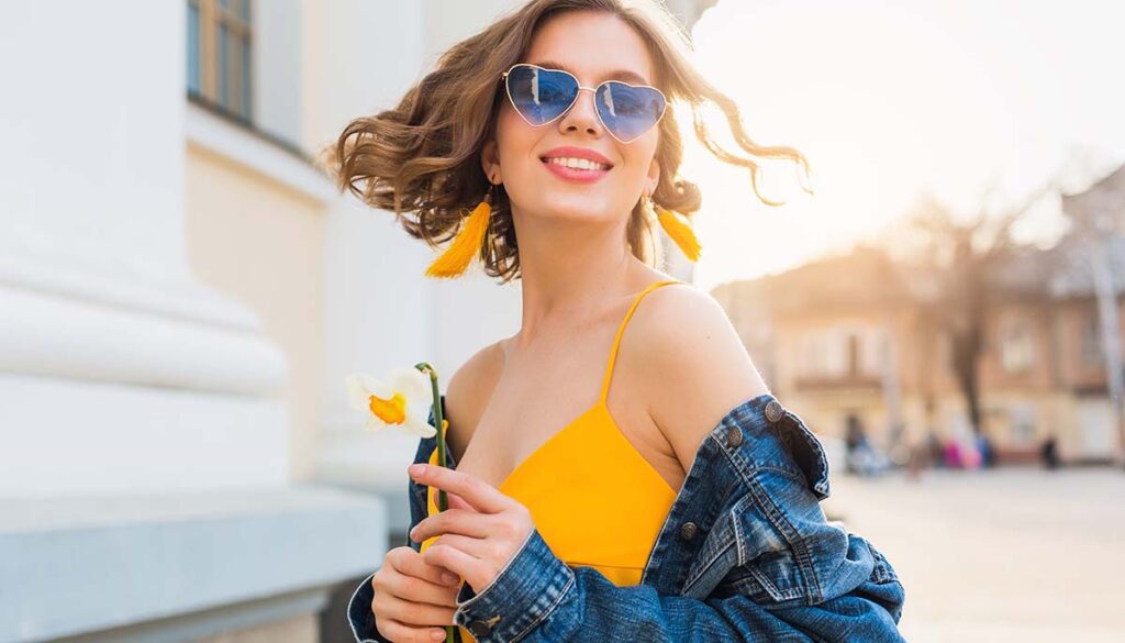 young woman smiling on street wearing heart shaped sunglasses