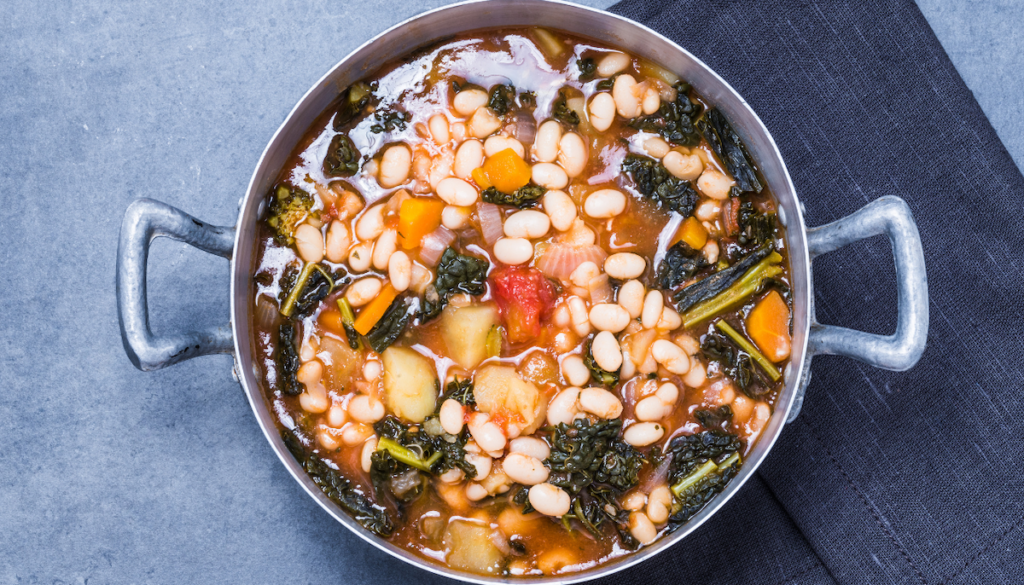 A pot of white bean and kale soup with assorted vegetables 