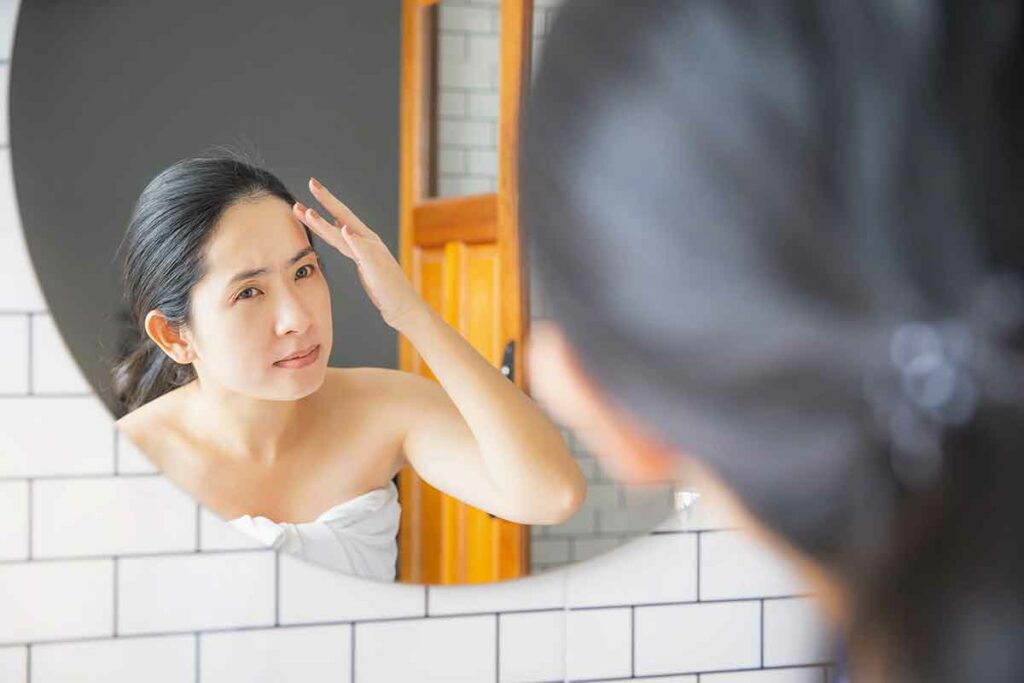 woman looking at her face in bathroom mirror