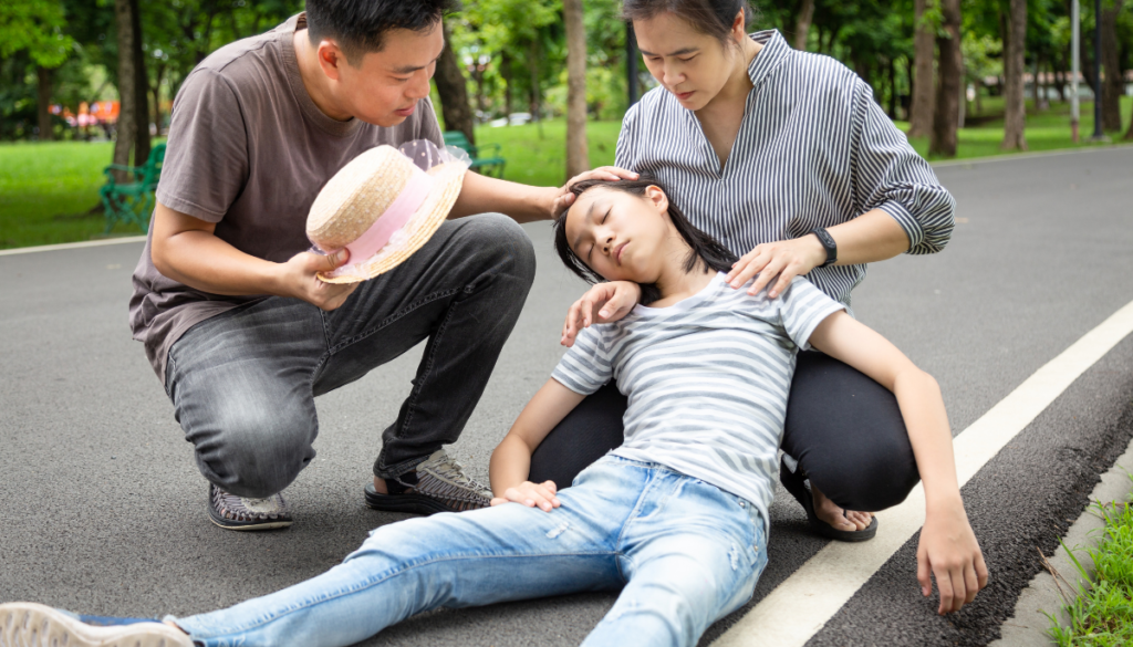 Young girl who fainted being held up by parents in park