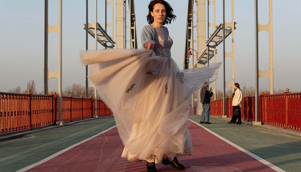 woman on bridge spinning in evening gown and casual shoes without makeup