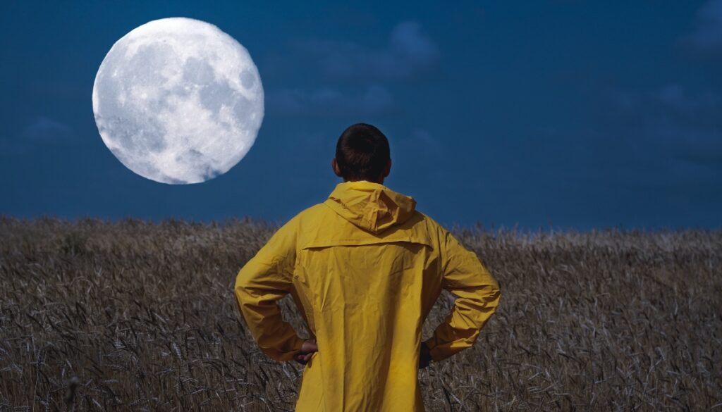 man in yellow jacket standing in front of a full moon