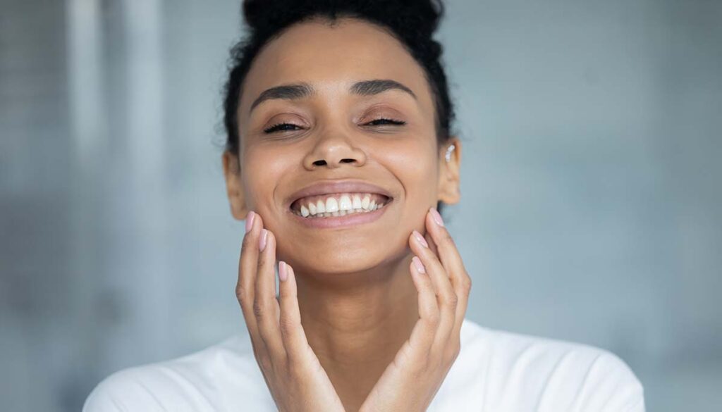 woman smiling and touching smooth skin on face