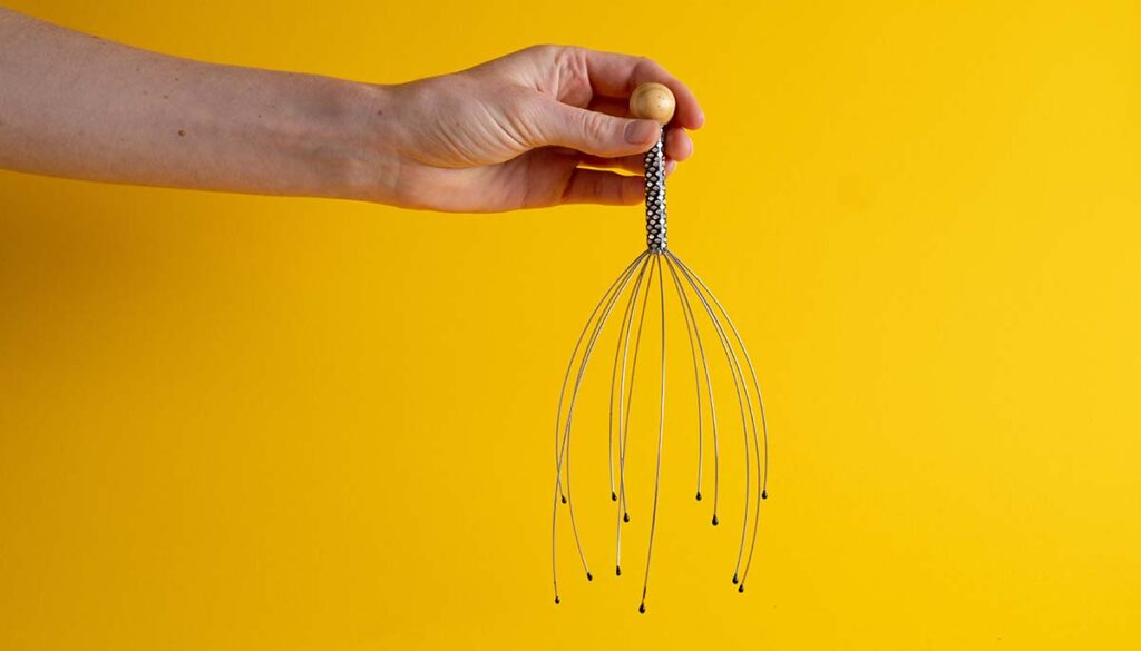 hand holding a scalp massager on yellow background