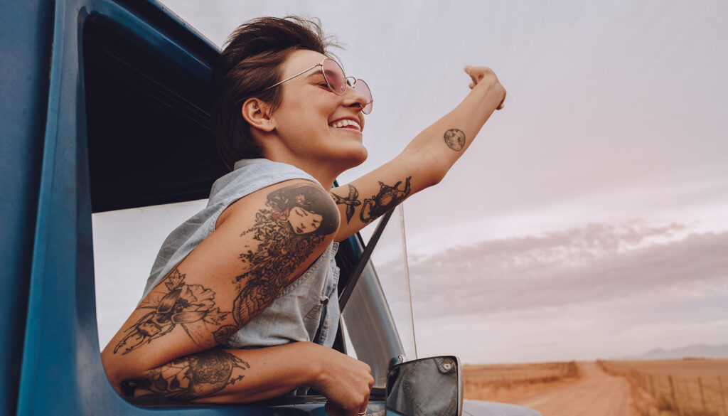 Shot of attractive young woman enjoying road trip on a summer day. Happy young female raising her hand out of the car window.