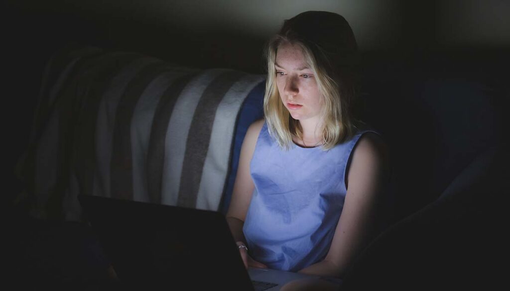 woman college student is fatigued from staying up all night staring at the screen of her laptop computer.