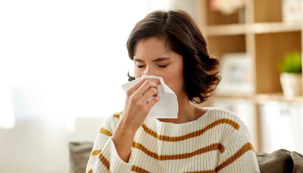 woman indoors sneezing into tissue