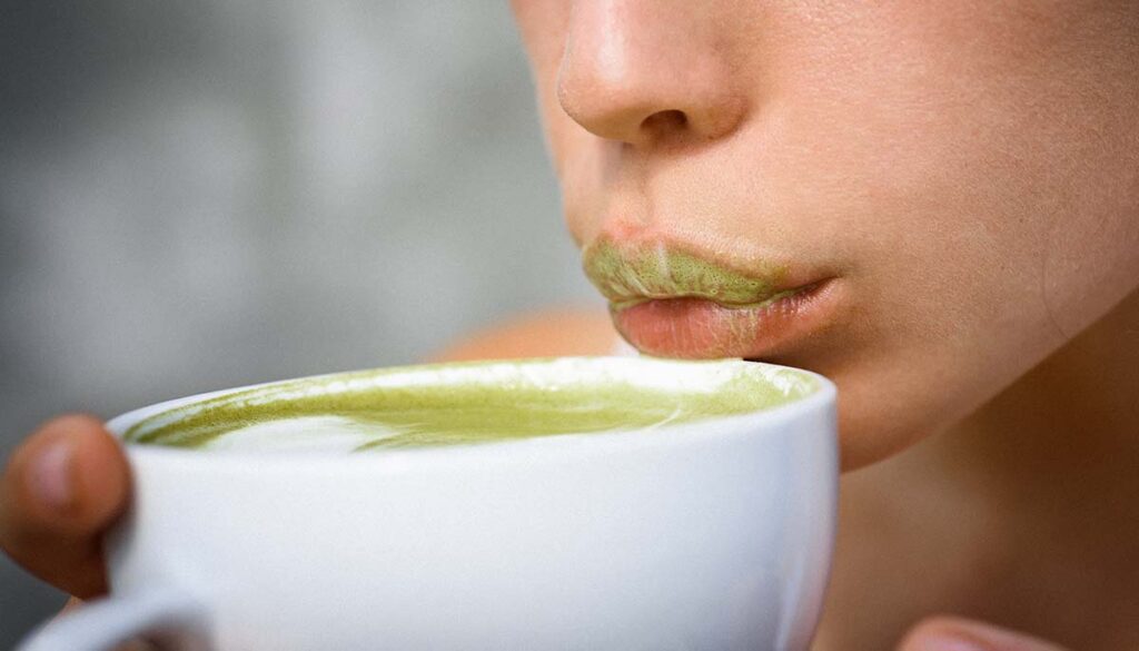 woman blowing on hot cup of matcha