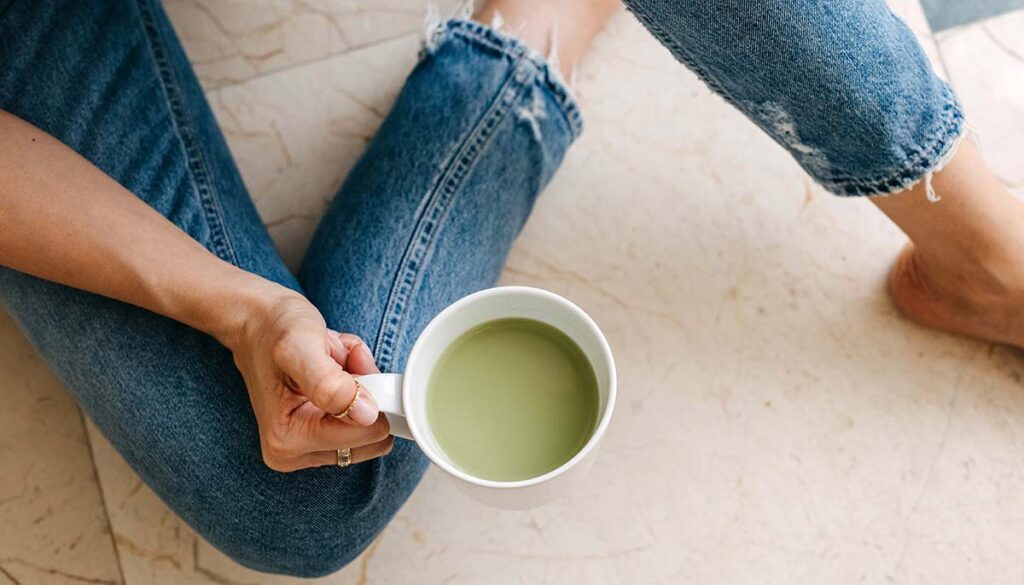 Close-up of a woman sitting on the floor, drinking matcha tea.