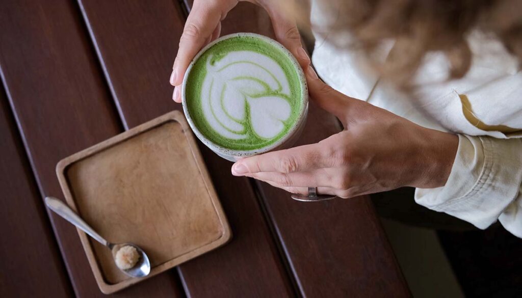 w of woman holding in hands trendy green matcha drink with heart shaped latte art