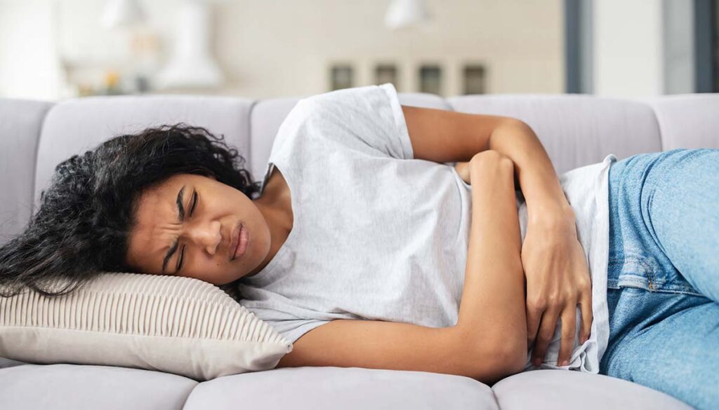 woman laying on couch cradling stomach suffering from cramps