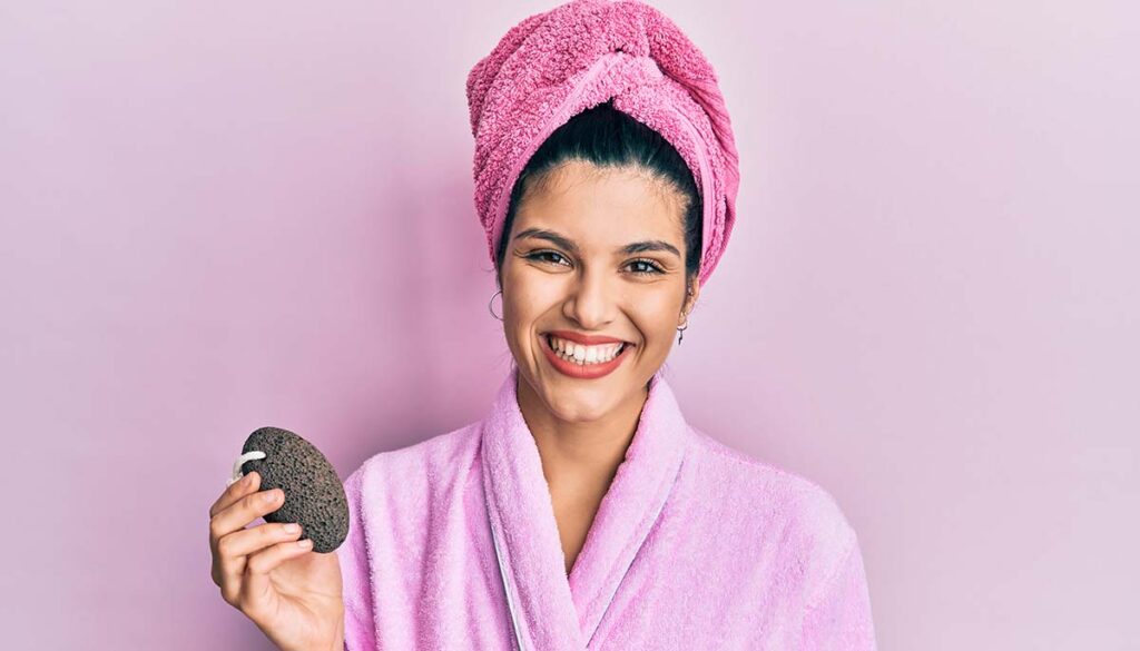 woman wearing shower bathrobe holding pumice stone looking positive and happy standing and smiling 