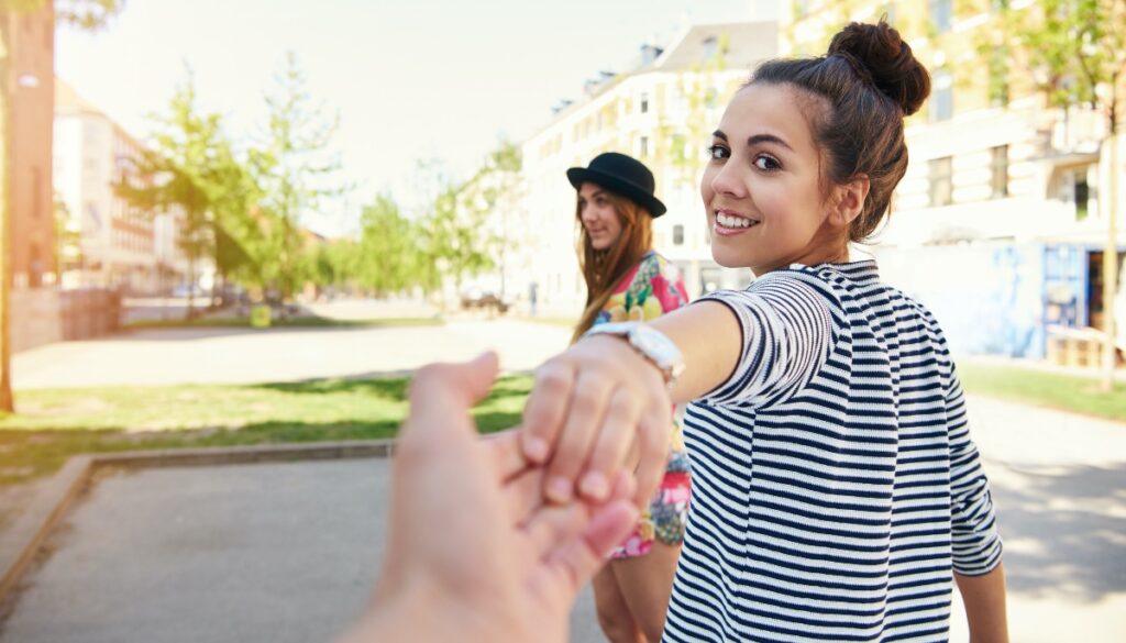 friends holding hands with other friend in the background