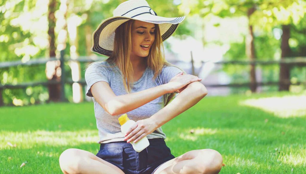 woman sitting in grass putting on sunscreen