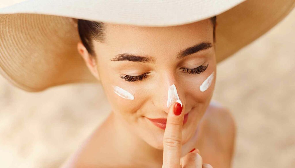 woman in hat putting on sunscreen