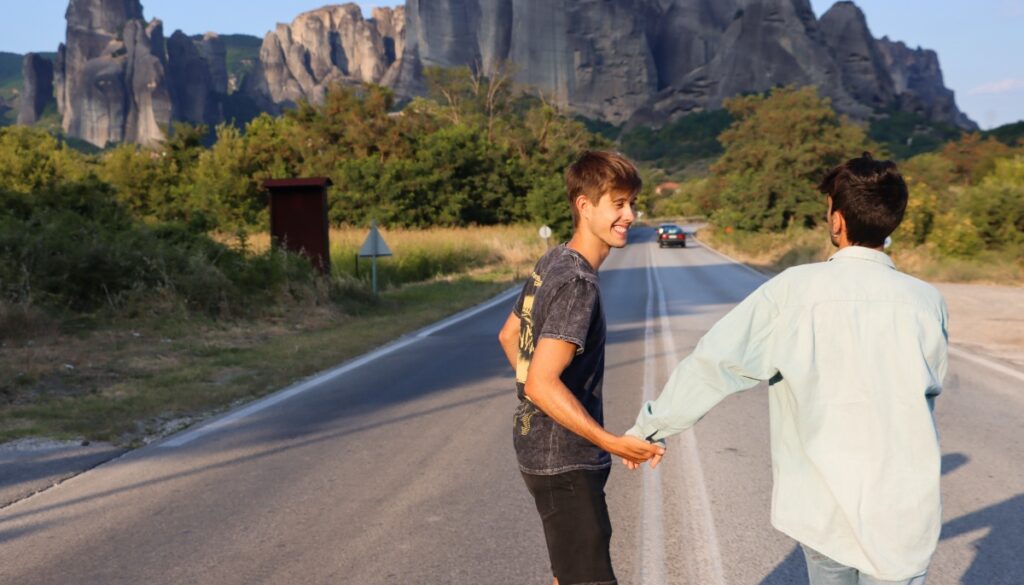 boyfriends holding hands on the road in front of a mountain