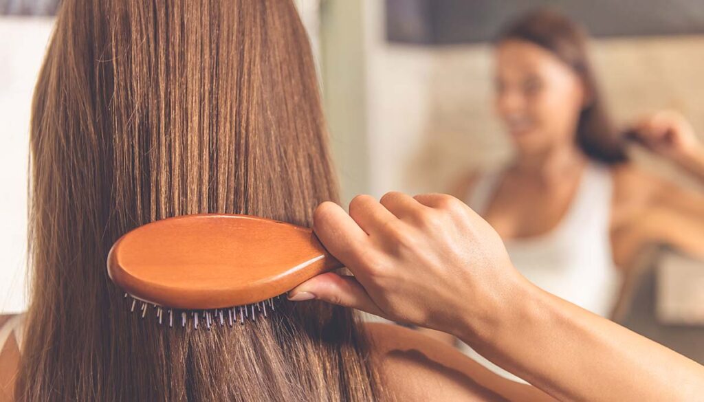 back of head of woman using hair brush and looking in the mirror