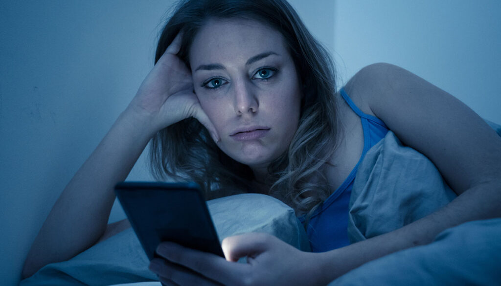 Bored woman looking at her phone instead of sleeping