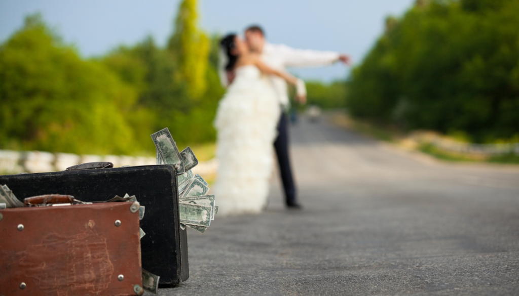 Suitcases with money in the foreground and couple on wedding day in background
