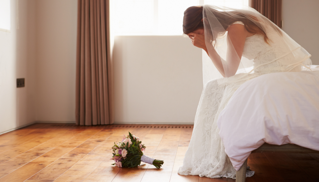Stressed bride sitting on bed with her head in her hands