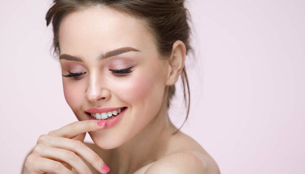 woman on blush pink background with pink nails touching her lips
