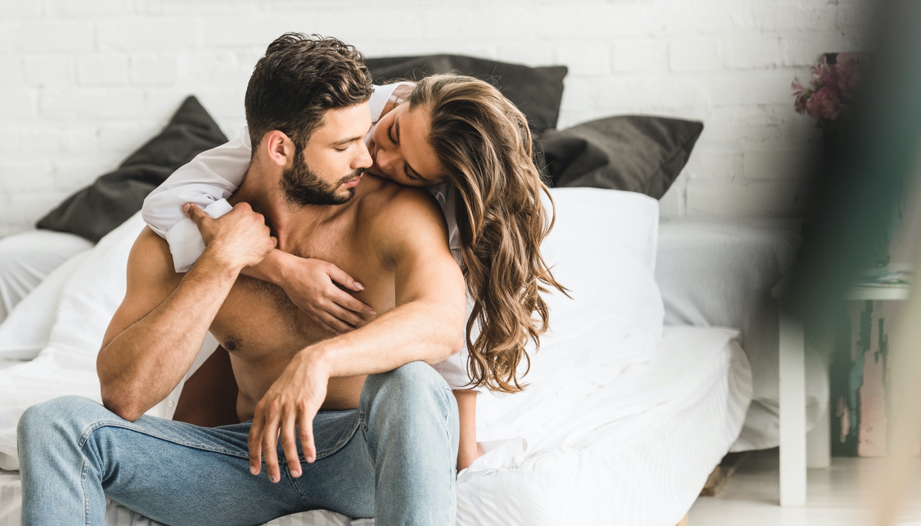 woman hugs man while sitting on a bed