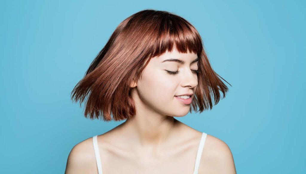 woman with shorter hair and bangs on blue background
