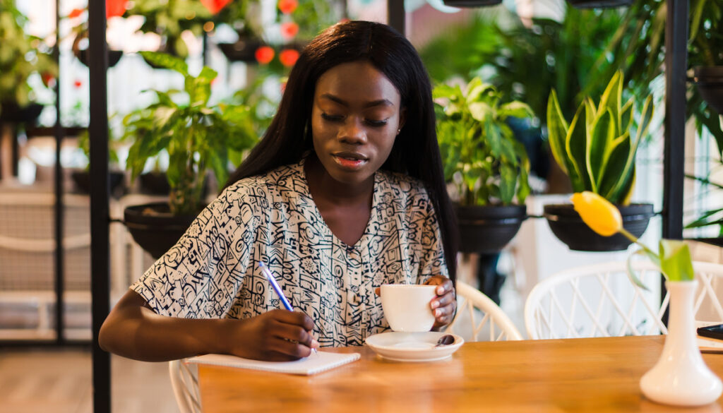 Young woman writing at cafe and drinking tea