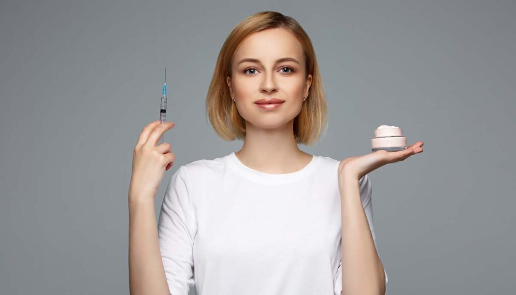 Woman holding face cream and syringe with beauty injection in hand, choosing skin care products. 
