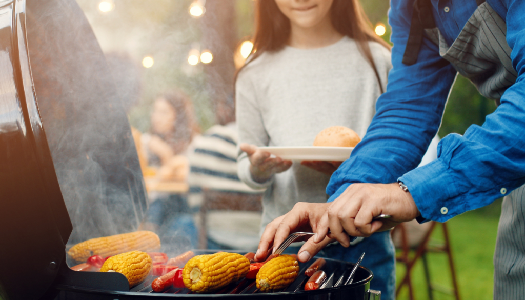 Person in blue shirt grilling corn on the cob
