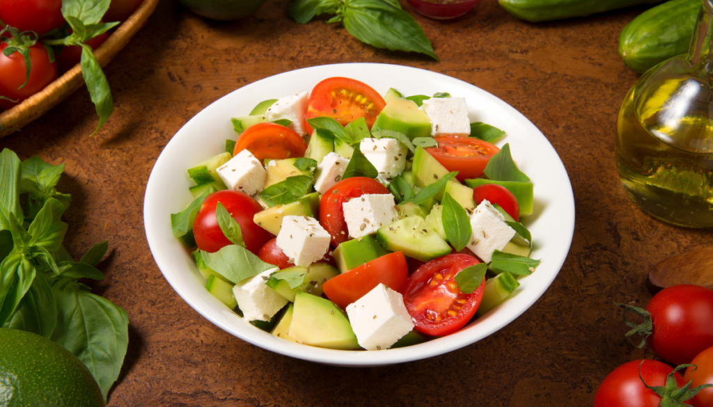 Avocado and cherry tomato salad with chunks of feta in white bowl on brown table