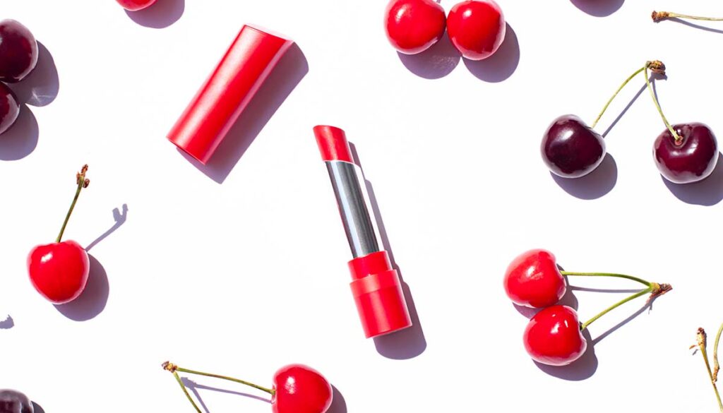 Red lipstick on the white background with ripe cherries. 