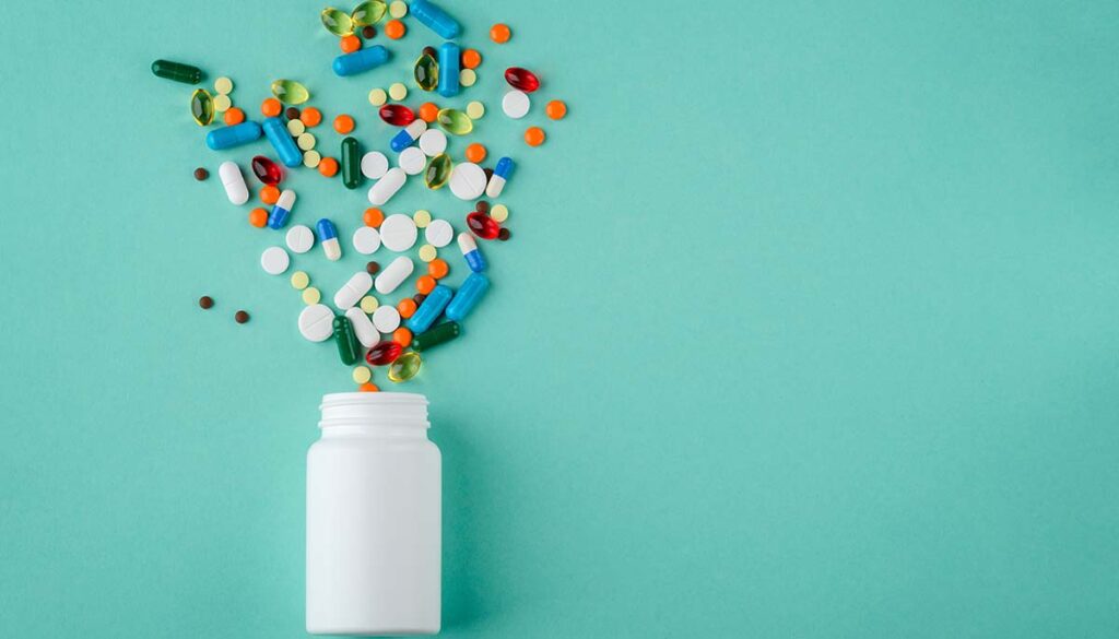 Various medications and vitamins spilling out of a pill bottle.