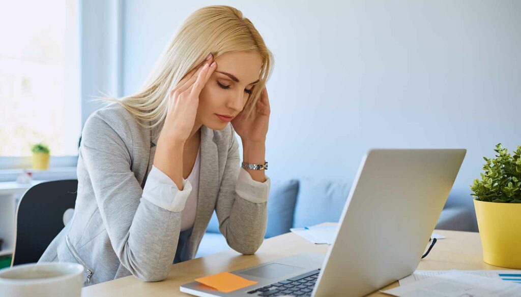 woman sitting at laptop, working, holding head in hands