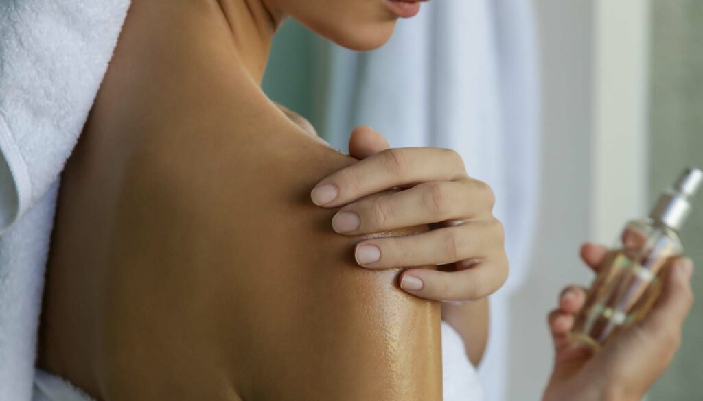 Woman applying body oil to moisturize her skin after shower