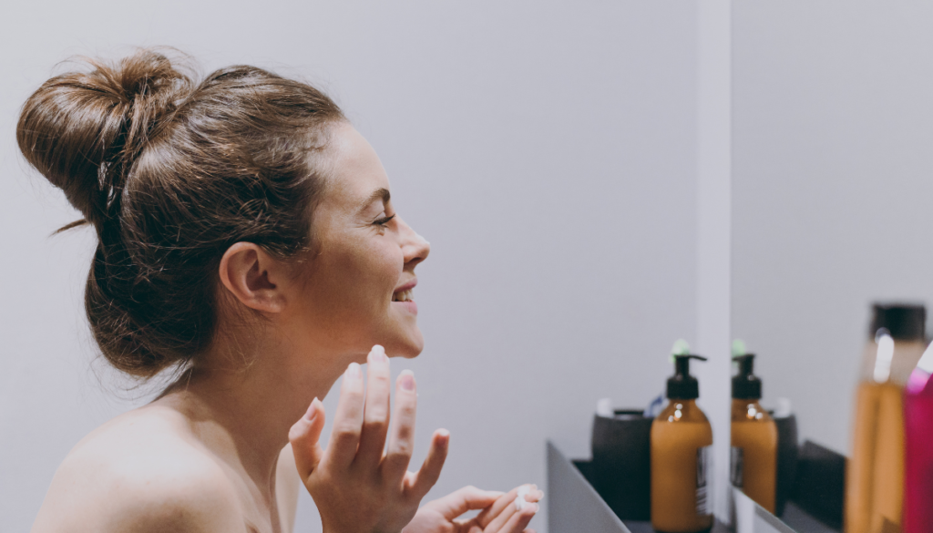 Smiling woman touching face while looking in bathromo mirror