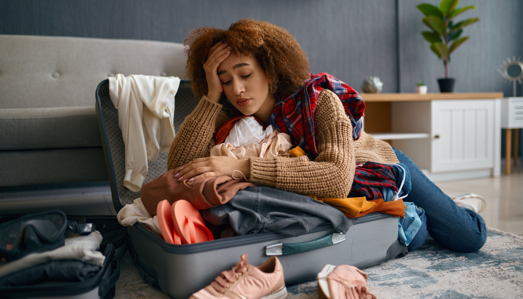 Sad woman sitting with arms on top of open messy suitcase