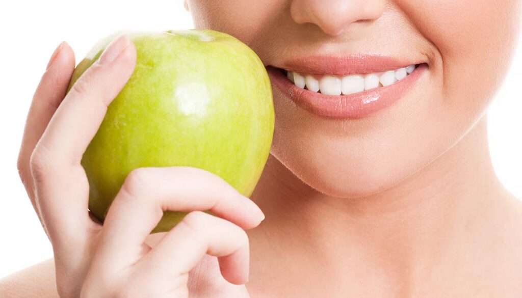 closeup of the face of a woman holding a green apple, isolated against white background