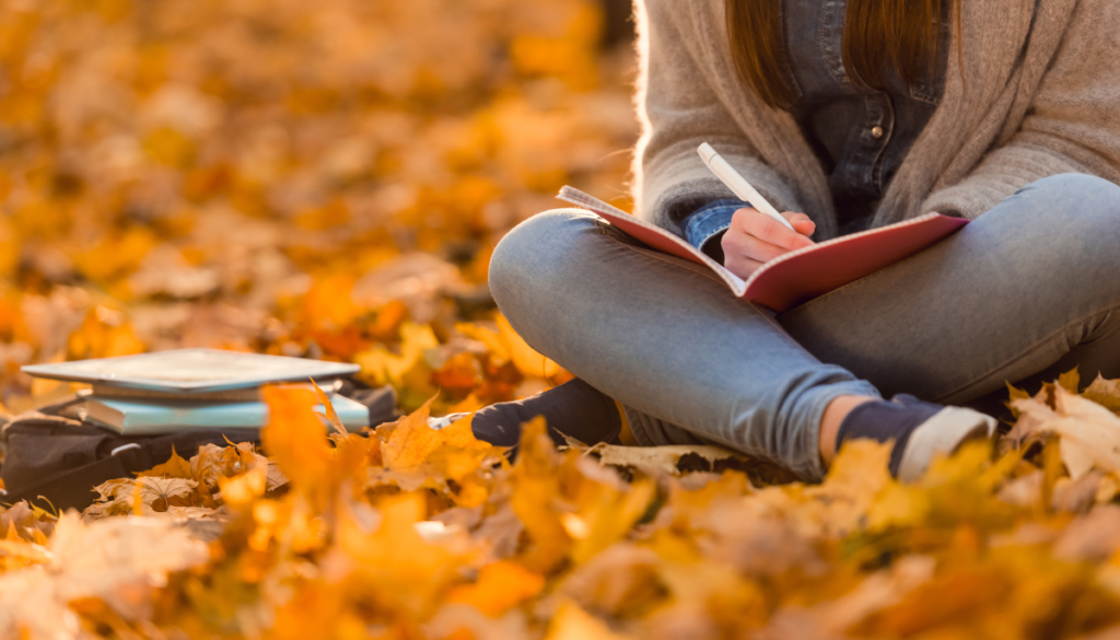 Woman sitting outside and writing in journal surrounded by orange leaves