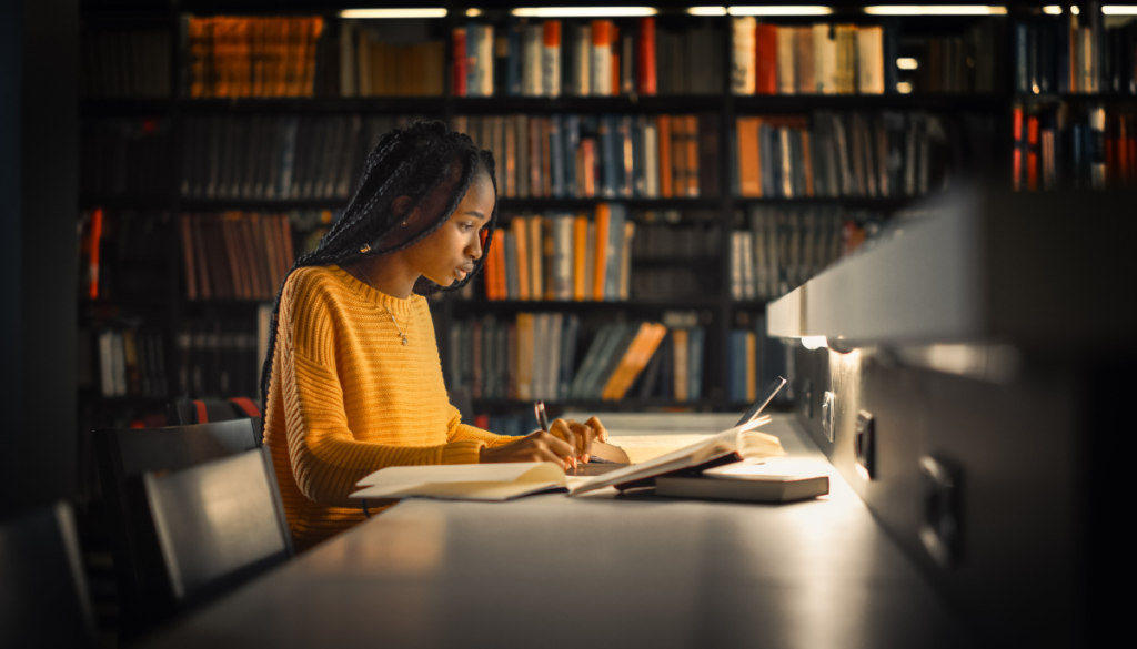 Young woman studying at long table in library at night