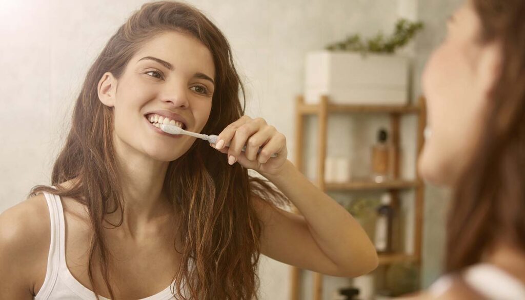 woman brushing teeth in the mirror